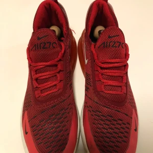 Röda Nike Air Max 270 - Snygga röda Nike Air Max 270 med en modern design och bekväm passform. Skorna har en synlig Air-enhet i hälen för extra dämpning och komfort. Perfekta för både träning och vardag.