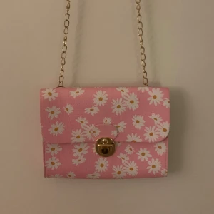 Rosa blommig axelväska  - Söt rosa axelväska med blommigt mönster och guldfärgad kedja. Köpt second hand men tror den kommer från shein ursprungligen. Mycket bra skick förutom att det finns ett visst slitage på själva låset. 18x 14,5 cm i diameter💗🎀