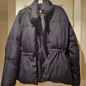 Svart pufferjacka från Zink - Säljer en svart pufferjacka från Zink. Jackan har en hög krage och dragkedja framtill. Perfekt för kyliga dagar med sin vadderade design.