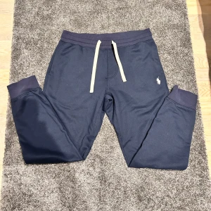 Ralph lauren mjukisbyxor - Snygga mörkblå mjukisbyxor från Polo Ralph Lauren med vit snörning i midjan och det klassiska logotypbroderiet på sidan. Sitter mer som M. Perfekta för en avslappnad stil.