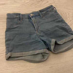 Blå jeansshorts från &Denim - Säljer ett par klassiska blå jeansshorts från &Denim. De har en normal passform med upprullade benslut och femficksdesign. Perfekta för en avslappnad stil.