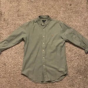 Ralph Lauren skjorta  - Säljer en stilren grön skjorta från Ralph Lauren i slim fit. Skjortan har långa ärmar och är tillverkad i stretchigt material för extra komfort. Den har klassiska knappar och en broderad logotyp på bröstet. Perfekt för en snygg och avslappnad look.