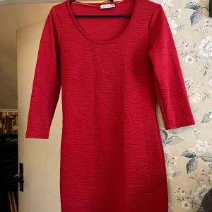 Röd klänning från Fransa - Snygg röd klänning från Fransa med trekvartsärm och rund halsringning. Perfekt för både vardag och festliga tillfällen. Klänningen har en enkel och stilren design som gör den lätt att matcha med olika accessoarer.