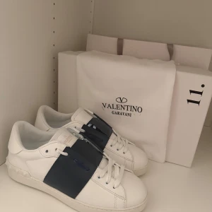 Valentino Opens - Snygga Valentino Opens sneakers i utmärkt skick. vita med en bred mörkblå rem över ovansidan. Skorna har klassisk snörning och är tillverkade i skinn. Perfekta för en stilren look. Dustbag, låda och påsen följer med. Tveka inte att höra av er vid minsta fundering. Pris kan diskuteras vid snabb affär