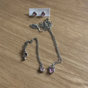 Smyckeset med rosa stenar - Elegant smyckeset bestående av ett halsband, armband och örhängen i silverfärg med rosa stenar. Oanvända! 