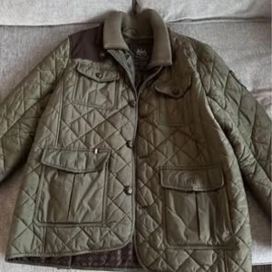 Olivgrön quiltad jacka från Morris - Snygg olivgrön quiltad jacka från Morris med knappar och flera praktiska fickor. Jackan har en stilren design med en mönstrad insida och är perfekt för höst- och vårsäsongen.