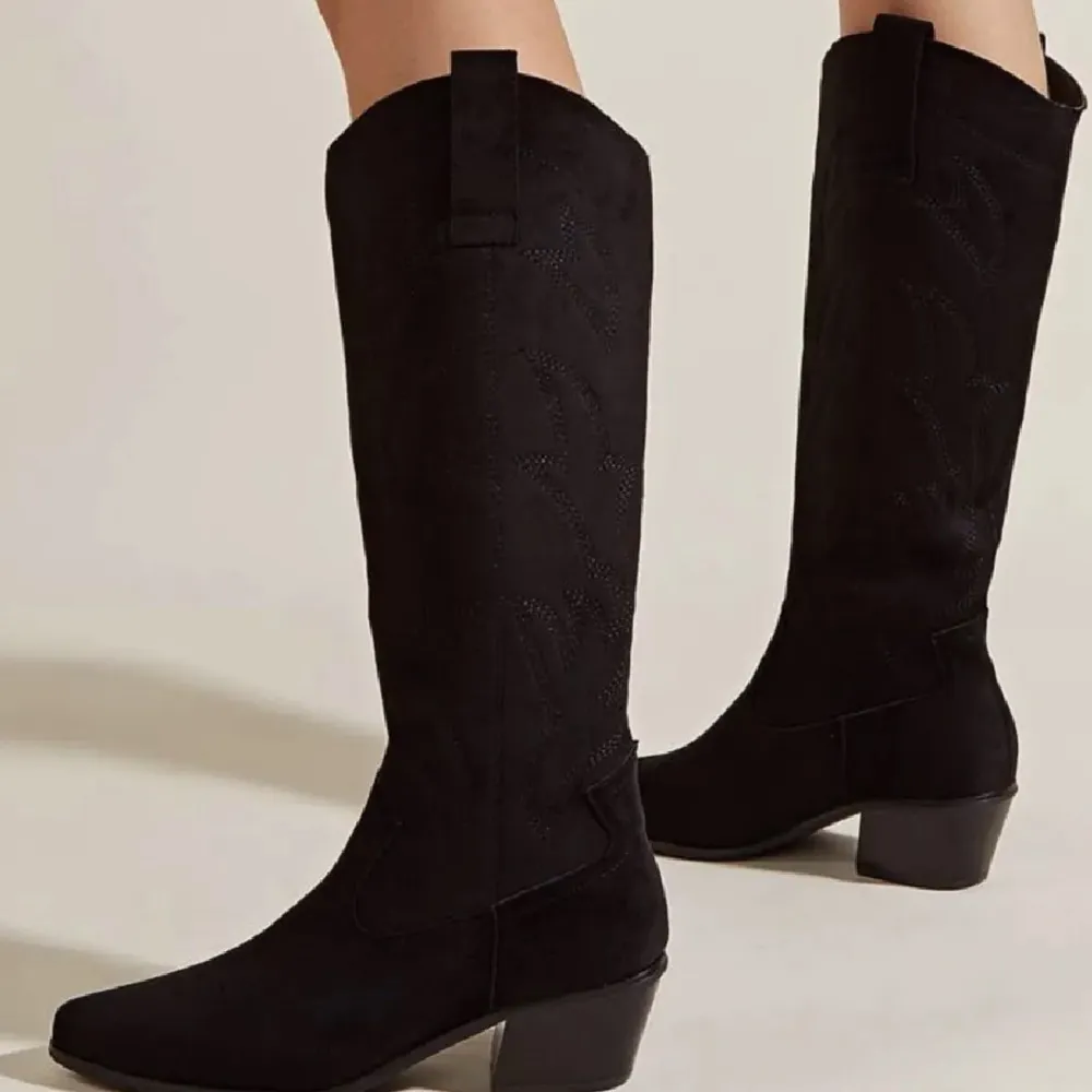 Säljer ett par snygga svarta cowboy boots i mocka. De har en klassisk design med spetsig tå och en liten klack som ger en cool look. Perfekta för höst och vinter, och funkar lika bra till fest som till vardags. De är i nyskick och redo för nya äventyr!. Skor.