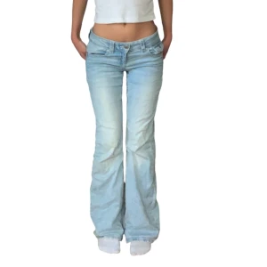Ljusblå bootcut jeans - Säljer ett par snygga ljusblå bootcut jeans i lågmidjad stil. De har en klassisk femficksdesign med knappar på bakfickorna. Passar mig bra som är 163