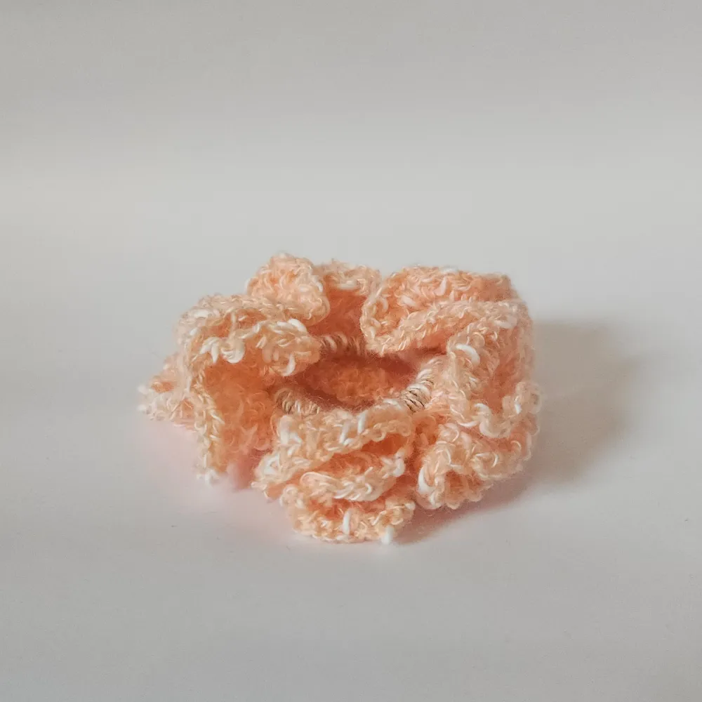 En superfin persikofärgad scrunchie som är virkad och perfekt för att ge en söt touch till din frisyr. Den är mjuk och elastisk, vilket gör den bekväm att bära hela dagen. Perfekt accessoar för både vardag och fest!. Asusteet.