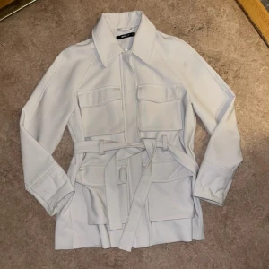 Beige kappa  - Jätte fin beige kappa med knytband.  Storlek 34.  Inköpt på Gina tricot förra året.  Är i jätte fint skick utan skavanker. 