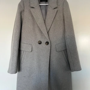 Grå ullkappa, Stradivarius, S - Grå ullkappa från Stradivarius i storlek S i mycket bra skick, då ej använd så mycket.  Material: 66% polyester, 24% ull, 10% övriga fiber. Foder 100% polyester.  Mått: Längd ca 92 cm Midja ca 45 cm Ärmlängd ca 63 cm Plagget kommer från ett djur- och