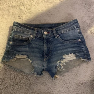 Blå jeansshorts med slitna detaljer - Säljer ett par coola blå jeansshorts med slitna detaljer och fransar. De har en klassisk femficksdesign och knappgylf. Orginalpris:400 knappt använd