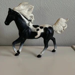 Leksaks häst - Säljer en detaljerad hästfigur i svart och vitt. Hästen har en elegant pose med fladdrande man och svans. Perfekt för samlare eller som dekoration.