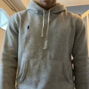 Grå hoodie från Ralph Lauren - Säljer en stilren grå hoodie från Ralph Lauren med det klassiska logotypen broderad på bröstet. Tröjan har en känguruficka och justerbar huva med snören. Perfekt för en avslappnad look. Endast 899 nypris 2400 Passar M men även S