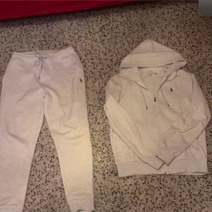 Grå hoodie och byxor från Polo Ralph Lauren - Säljer en stilren grå hoodie från Polo Ralph Lauren med dragkedja och det klassiska logotypbroderiet på bröstet. Perfekt för en avslappnad look. Den har en justerbar huva och långa ärmar. Med byxor 
