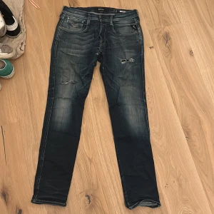 Blå jeans från Replay - Säljer ett par snygga blå jeans från Replay med slitna detaljer och en klassisk femficksdesign. De har en dragkedja och knapp framtill. Perfekta för en avslappnad stil. Pris kan diskuteras 