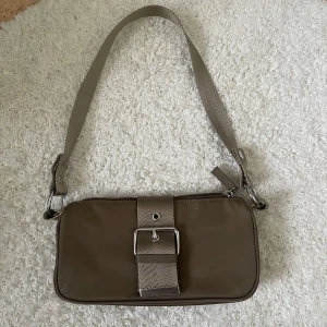 Hand/axelväska - Liten hand/axelväska från Weekday. I en brun/champagne färg. Helt oanvänd & i nyskick. 150kr