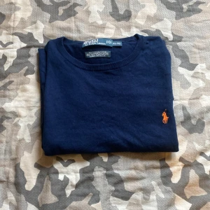 Mörkblå tröja från Polo Ralph Lauren - Säljer en mörkblå tröja från Polo Ralph Lauren med det klassiska broderade logotypen i orange på bröstet. Tröjan har långa ärmar och ribbade muddar. Perfekt för en stilren look.