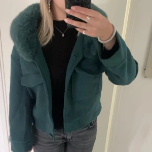 meotine liknade jacka - Snygg grön jacka med fluffig pälsdetalj på kragen. Jackan har en croppad passform och stora fickor framtill. älskar denna jacka men säljer för den är lite för kort i armarna och kommer ej till användning💕