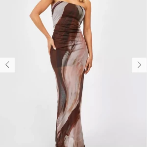Axelbandslös klänning från Boohoo - Snygg axelbandslös klänning från Boohoo med ett abstrakt mönster i bruna och beige toner. Klänningen är lång och har en figurnära passform som framhäver silhuetten. Perfekt för en elegant kvällslook. Oanvänd då den var för liten.