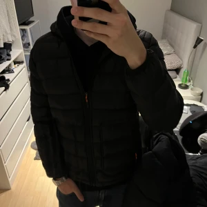 Svart pufferjacka från Vintage Denim - Säljer en svart pufferjacka från Vintage Denim. Jackan har en quiltad design med dragkedja och huva. Perfekt för kyligare dagar med sin stilrena look och bekväma passform. 