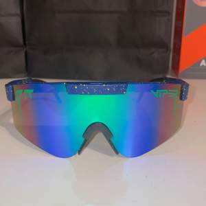Snygga blå solglasögon från Pit Viper med spegelglas i grönt och blått. Bågarna har ett coolt stänkmönster i gult och justerbara skalmar för perfekt passform. Perfekta för en sportig look!