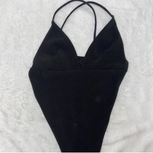 Svart ärmlös body med korsade band - Snygg svart ärmlös body med korsade band i ryggen. Perfekt för en stilren och modern look. Passar bra till både byxor och kjol. Den har en söm längs me ryggen som man ser att den e handsydd om man kollar noga