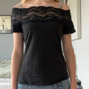 Svart offshoulder topp med spetsdetaljer - Snygg svart offshoulder topp med spetsdetalj över axlarna. Står inte storlek i men jag skulle säga att den är S.