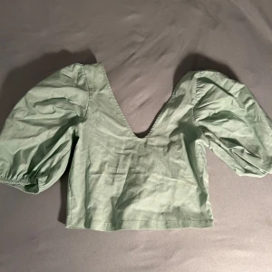 Grön crop top med puffärmar - Säljer denna festliga gröna crop top från Pull & Bear med  v-ringning och puffiga ärmar. Den har en elastisk detalj i ryggen för bättre passform. Perfekt för en varm sommardag eller till festen. Toppen är endast använd ett fåtal gånger men jag säljer den då den tyvärr inte kommer till användning. Kontakta mig för mer information.💚