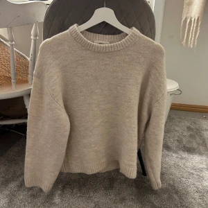 Beige stickad tröja - Mysig beige stickad tröja med rund hals och långa ärmar. Perfekt för kyliga dagar och enkel att matcha med olika outfits. Tröjan har en klassisk design med ribbade kanter vid ärmslut och nederkant.