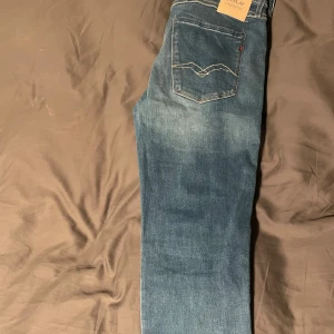Replay anbass hyperflex, blåa - Snygga blå jeans från Replay med klassisk femficksdesign och dragkedja. De har en normal passform och är perfekta för en avslappnad stil. Märkesdetaljer syns på fickorna och bältet.