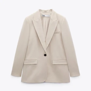 Beige kavaj från Zara - Elegant beige kavaj från Zara med klassisk design. Kavajen har en enkel knapp framtill och två fickor med lock. Perfekt för en stilren look.