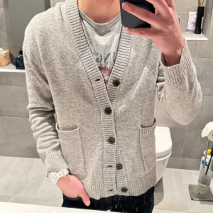 Grå kofta med knappar - Säljer en stilren grå kofta med knappar framtill. Den har långa ärmar och två praktiska fickor. Perfekt för en avslappnad look. Endast använd en gång!