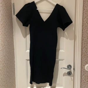 Svart klänning från Vero Moda - Elegant svart klänning från Vero Moda med v-ringning och korta ärmar. Perfekt för en stilren look. Klänningen har en figurnära passform, bara använd en gång så är i bra kondition! 