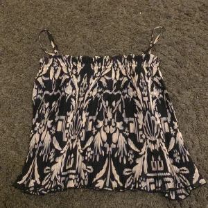 Mönstrad topp från H&M - Säljer en snygg mönstrad topp med smala axelband. Toppen har ett mörkblått och vitt mönster och är perfekt för varma dagar. Den är ärmlös och har en luftig passform.