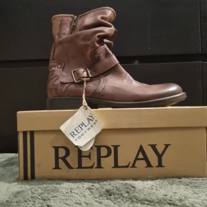 Bruna boots från Replay - Snygga bruna boots från Replay med dragkedja och dekorativt bälte. Tillverkade i skinn med en robust design. Perfekta för en stilren look.orginal pris 3000 kr så det är en jätte bra deal