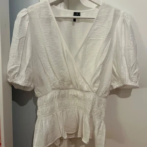 Vit omlottblus från Vero Moda - Säljer en stilren vit omlottblus från Verp Moda med korta puffärmar och elastisk midja. Blusen är perfekt för både vardag och fest. Passar bra till jeans eller kjol.