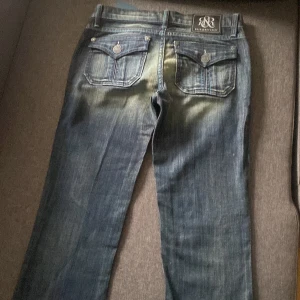Blå jeans från Rock & Republic - Snygga blå jeans från Rock & Republic med coola detaljer som knappar och fickor bak. Jeansen har en klassisk femficksdesign och en mörk tvätt med ljusare partier för en trendig look. Perfekta för att ge din outfit en edgy touch. Och även botcut helt nya köpta för 1500 priset kan diskuteras 