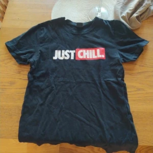 Svart t-shirt med tryck från FSBN - Säljer en svart t-shirt från FSBN med texten 'JUST CHILL' i vitt och rött tryck på framsidan. T-shirten har en normal passform och är kortärmad, perfekt för en avslappnad stil.