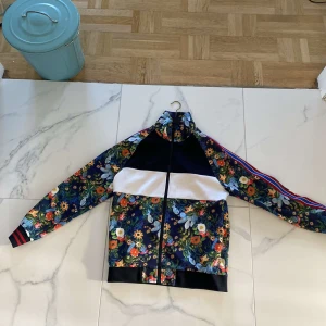 Blommig jacka från Zara Man - Säljer en supercool blommig jacka från Zara Man. Den har en färgglad blommig design med inslag av blått, grönt och orange. Jackan har en dragkedja framtill och långa ärmar med randiga muddar. Perfekt för att sticka ut i mängden!