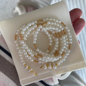Långt halsband att bära på flera olika sätt  - Långt pärlat halsband som går att bära på flera olika sätt. Pärlat med vita och guldiga pärlor samt sötvattenspärlor. Kommer i en vit sammetspåse. Perfekt gåva till sig själv eller att ge bort. 