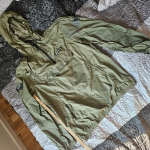 Grön vindjacka från Ellesse - Säljer en grön vindjacka från Ellesse. Den är perfekt för vår och höst med sin lätta och smidiga design. Jackan har en huva och en praktisk dragkedja framtill. Den är tillverkad i 100% nylon vilket gör den både slitstark och bekväm. Perfekt för en casual look eller när du behöver något lätt att slänga på dig. Skick efter bilder, inga hål iallafall.