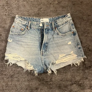 Blå jeansshorts från Zara - Snygga blå jeansshorts från Zara med slitna detaljer och fransig kant. Knappt använda så därför inte alls speciellt slitna! Säljer på grund av att de är för små. Storlek 36 men kan upplevas som 32/34! 💕