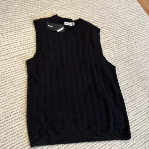 Svart stickad väst från Weekday - Snygg svart stickad väst från Weekday i en oversized passform. Västen har ett ribbat mönster och är perfekt för lager-på-lager-stil. Den är ärmlös och har en rund halsringning. Perfekt till sommaren med en vit t-shirt under. Aldrig använd prislapp kvar. 