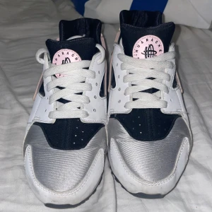 Nike sneakers i svart, vitt och silver - Snygga Nike sneakers med en cool kombination av svart, vitt och silver. Skorna har en unik design med rosa detaljer och snörning. Perfekta för en sportig look.