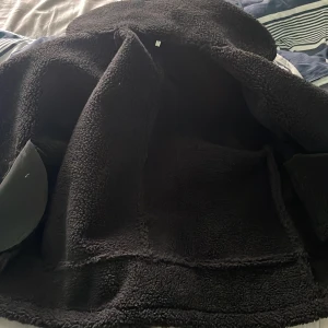 Svart teddyjacka med skinn - Säljer en svart teddyjacka med skinnytor och dragkedja. Jackan har en mysig teddyfoder och långa ärmar. Perfekt för kyliga dagar. Jacka är köpt i Kina för 700kr helt ny litten för mey .