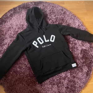 Svart hoodie från Ralph Lauren - Snygg svart hoodie från Ralph Lauren med stor POLO-logga på bröstet. Tröjan har en praktisk magficka och justerbar huva med snören. Perfekt för en avslappnad stil. Något nopprig men går säkert att fixa, annars helt perfekt skick. Skriv vid frågor eller funderingar!🤩