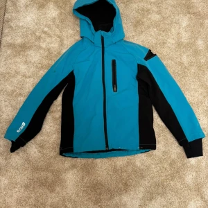 Blå och svart jacka från H&M storlek 152 - Turkos och svart jacka med huva storlek 152. Jackan har en dragkedja fram och en ficka på bröstet med dragkedja. Det finns en liten fläck på ärmen.  Kön: pojke men passar unisex Skick 8/10 se bilder Märke: H&M  Din stil: spara inlägget så du inte missar denna kappa Inte din stil: Kolla min profil. Du kommer hitta något för alla kön och åldrar.