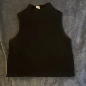 Svart ärmlös topp  - Snygg svart ärmlös topp i en tight passform. Perfekt för lager-på-lager eller att bära som den är. Tillverkad i ett mjukt och stretchigt material för extra komfort.