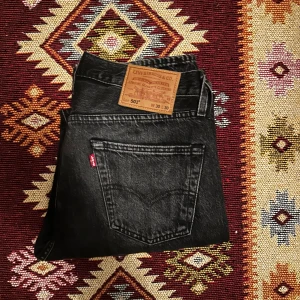 Svarta Levis 501 jeans - Snygga svarta Levis 501 jeans i klassisk design i nästintill nyskick. De har en rak passform och är tillverkade i slitstarkt denim. Perfekta för en stilren look med fem fickor och knappgylf. Priset går ner vid snabb affär!
